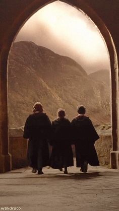 three people walking under an arch with mountains in the background