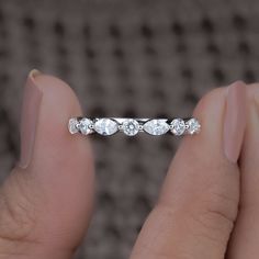 a woman's hand holding a wedding band with three diamonds on it, in front of a gray background