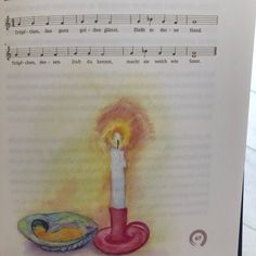 an open book with a lit candle next to a bowl of fruit and music notes