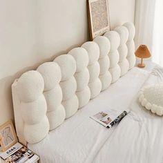 there is a white headboard on top of the bed with pillows and magazines next to it