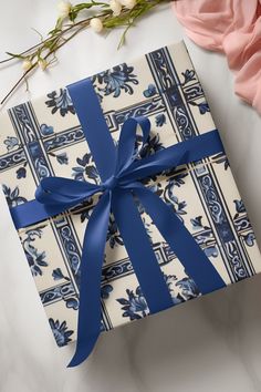 a gift wrapped in blue and white wrapping paper with a bow on it next to flowers