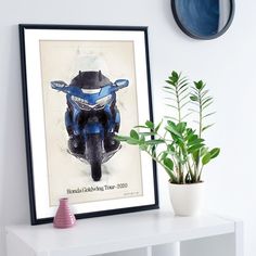 a blue motorcycle is on display next to a potted plant and a framed photograph