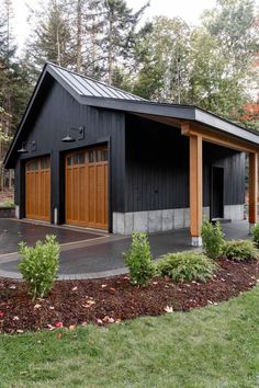 a black garage with two brown doors in front of trees and grass on the ground