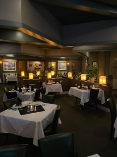 a dining room with tables and chairs covered in white tablecloths, lit by candles