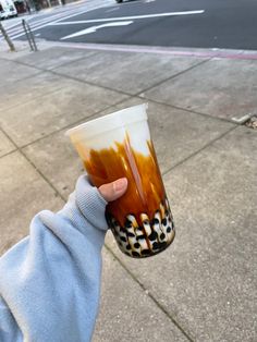 a person holding up a cup with liquid in it on the side of the road