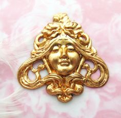 a gold brooch with a woman's face in the center on a pink and white background