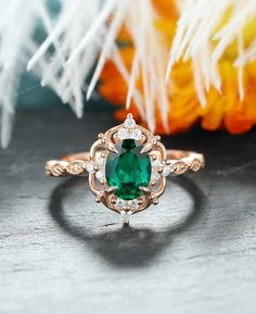 an oval cut emerald ring with diamond accents on a table next to flowers and feathers