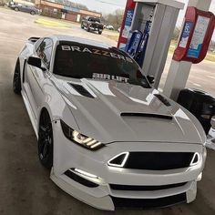 a white car is parked in front of a gas station with its hood up and lights on