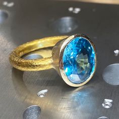 One-of-a-kind, hand-crafted ring centering 10.20 carat oval shape, fine gem quality vivid color Blue Zircon set in 18karat yellow gold bezel and 22karat yellow gold hammered setting. Size 7, can be sized upon request. Zircon might be one of the most under-appreciated colored gemstones and please do not confuse it with cubic zirconia, or CZ, an artificial product from the mid-1970s. Zircon found in Australia is the oldest mineral on earth: 4.4 billion years old. In the Middle Ages, this gem was t Gold Oval Topaz Ring With Bezel Setting, Unique Oval Yellow Gold Topaz Ring, Gold Blue Topaz Ring With Bezel Setting, Oval Yellow Gold Topaz Ring With Bezel Setting, Handmade Gold Topaz Ring In Oval Shape, Handmade Gold Topaz Ring With Oval Shape, 3d Printed Necklace, Royal Blue Sapphire Ring, Fine Jewelry Rings