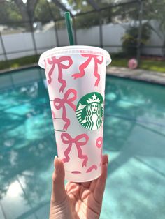 someone holding up a starbucks cup in front of a pool with pink bows on it