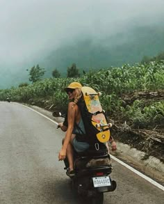 a man riding on the back of a motorcycle down a road with a surfboard strapped to his back