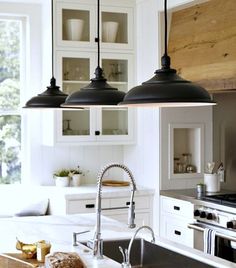 three lights hanging over a kitchen sink next to an oven and counter top with bread on it