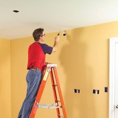 a man on a ladder painting the walls in a room that is being painted yellow