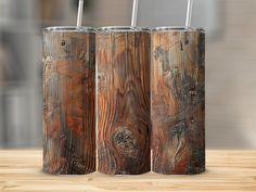 three wooden cans with metal straws in them on a wood table next to a brick wall