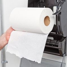 a person holding a roll of toilet paper in front of a machine with it's lid open