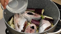 someone is pouring water over fish and vegetables in a pot