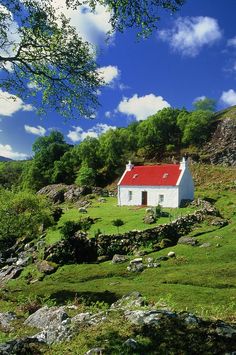 a white house with a red roof sitting on top of a lush green hillside