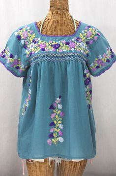 "* Ornate hand embroidery and smocking with hand crocheted trim on the neck and open sleeve hems, available here in POOL BLUE with PURPLE MULTI embroidery. * Light, gauzy and semi-sheer 100% cotton throughout; wear it billowy and flowing in the bohemian style, or belted for a more fitted look. * Dyed, distressed and embroidered by hand for an authentic, retro-vintage and boho-chic hippie vibe. * Our colorful and ornate floral embroidery patterns are a faithful tribute to the traditional hippie p Bohemian Light Blue Blouse With Floral Embroidery, Blue Tops With Embroidered Border For Spring, Peasant Top With Multicolor Embroidery, Folk Style Peasant Top With Multicolor Embroidery, Blue Cotton Peasant Top With Floral Embroidery, Traditional Blue Tops With Embroidered Border, Blue Peasant Tops With Floral Embroidery, Blue Folk Style Top With Embroidered Hem, Traditional Blue Peasant Top With Floral Embroidery