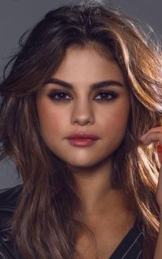 a beautiful young woman with long hair posing for the camera and holding her hand up to her face