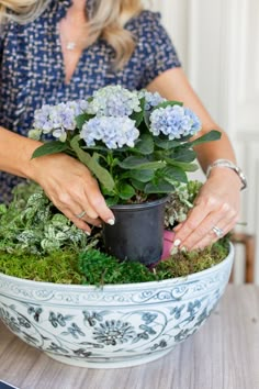 a woman holding a potted plant on top of a table