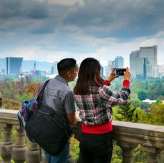 a man and woman standing on top of a balcony looking at the cityscape