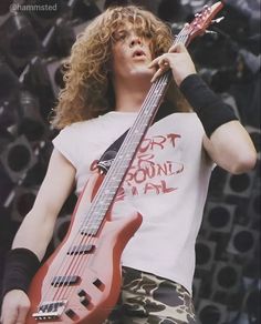 a man with long curly hair holding a red guitar in his right hand and looking up at the sky