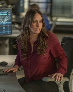 a woman sitting at a desk with a laptop computer in front of her and a monitor behind her