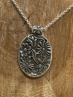 This gorgeous pendant is crafted using Fine Silver.  It features an array of flowers and leaves in an oval shape.  This pendant hangs on a 24inch Sterling Silver small Rolo chain. Artisan Oval Necklaces, Artisan Oval Engraved Necklace, Artisan Engraved Oval Necklace, Silver Oval Pendant Metal Jewelry, Silver Metal Necklace With Oval Pendant, Silver Oval Jewelry With Flower Charm, Nature-inspired Oval Engraved Necklace, Silver Necklace With Flower Charm Oval Pendant, Nature-inspired Oval Engraved Necklaces