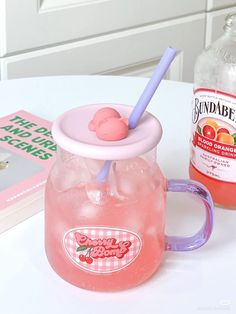 a pink drink with a straw in it next to a book on a white table