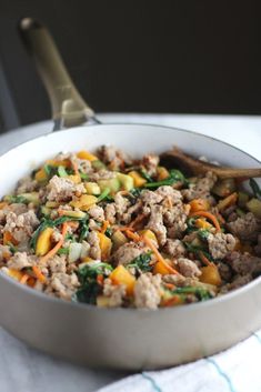 a white bowl filled with meat and vegetables on top of a table next to a spoon