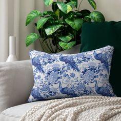 a blue and white pillow sitting on top of a couch next to a potted plant