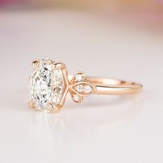 a close up view of a diamond ring on a white surface with pink flowers in the background