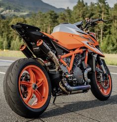 an orange and black motorcycle parked on the side of the road with mountains in the background