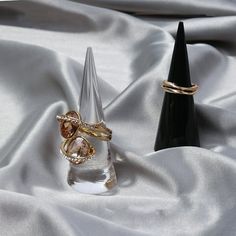 two gold rings sitting on top of a white satin covered table next to a black cone