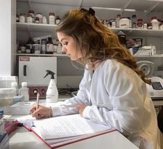 a woman in white lab coat writing on paper