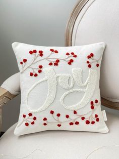 a white chair with a red and white pillow on it's back that says joy