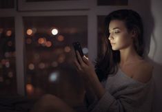 a woman sitting on the floor looking at her cell phone in front of a window