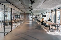 people are sitting at long tables in an open area with large windows and glass walls