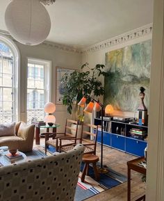 a living room filled with furniture next to a large painting on the wall and windows