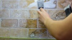 a person is painting a brick wall with white paint and a brush in their hand