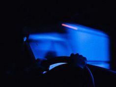 a person driving in the dark at night with their hands on the steering wheel, while using a cell phone