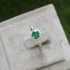 an engagement ring with a green stone surrounded by white diamonds on top of a box