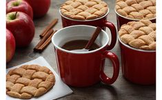 four red mugs with cinnamon cookies in them and cinnamon sticks on the table next to them