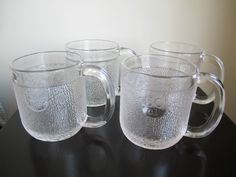 three clear glass mugs sitting on top of a black table next to each other