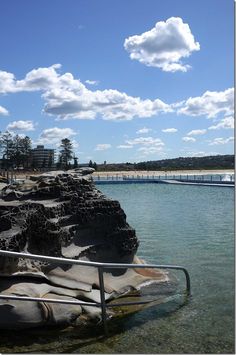 the water is crystal blue and there are clouds in the sky over the rocks on the shore