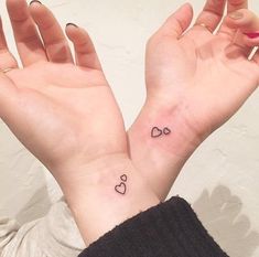 two hands with small tattoos on them, one has a heart and the other has a bow