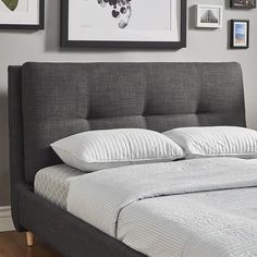 there is a bed with white pillows and gray headboard in the room next to pictures on the wall