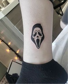 a person with a black and white mask tattoo on their left arm, showing it's tongue