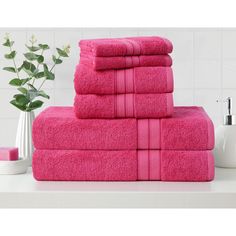 a stack of pink towels sitting on top of a white counter next to a vase