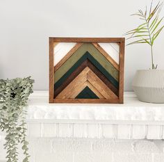 a wooden frame sitting on top of a white mantle next to a potted plant